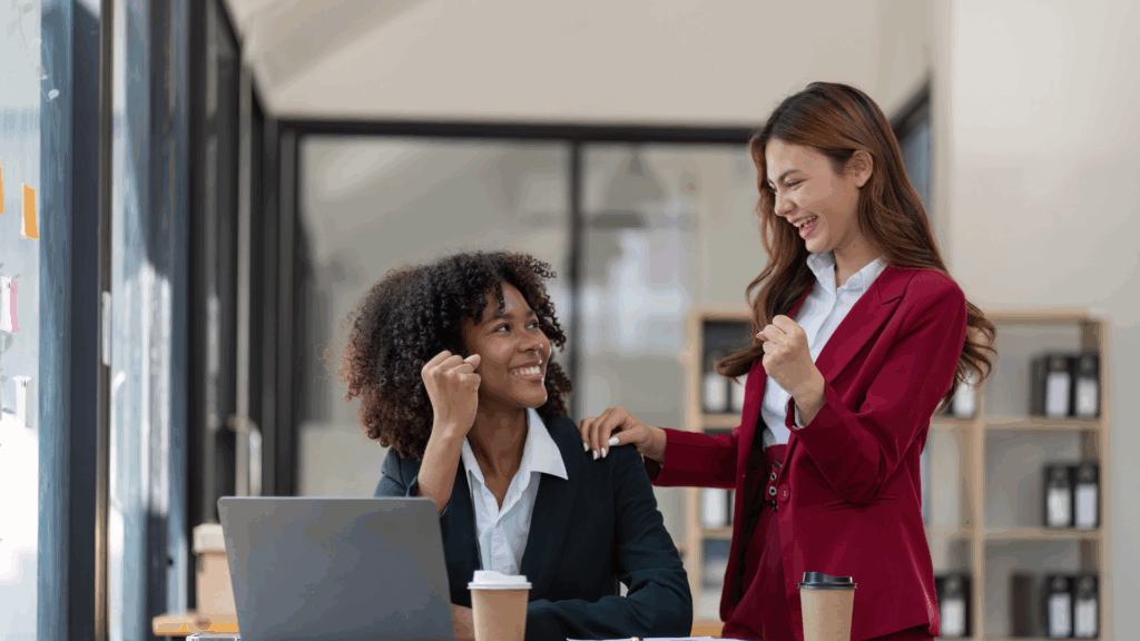 Obraz przedstawia dwie kobiety pracujące w&nbsp;nowoczesnym biurze.&nbsp;Jedna z nich,&nbsp;ubrana w&nbsp;bordową marynarkę,&nbsp;wspiera drugą gestem dłoni na jej ramieniu.&nbsp;Kobieta siedząca przy biurku wygląda na zamyśloną i&nbsp;niepewną,&nbsp;a&nbsp;przed nią stoi laptop i&nbsp;kubek kawy.&nbsp;Sceneria biurowa symbolizuje wsparcie i&nbsp;rozmowę o trudnościach związanych z brakiem pewności siebie oraz o zjawisku,&nbsp;jakim jest syndrom oszusta.