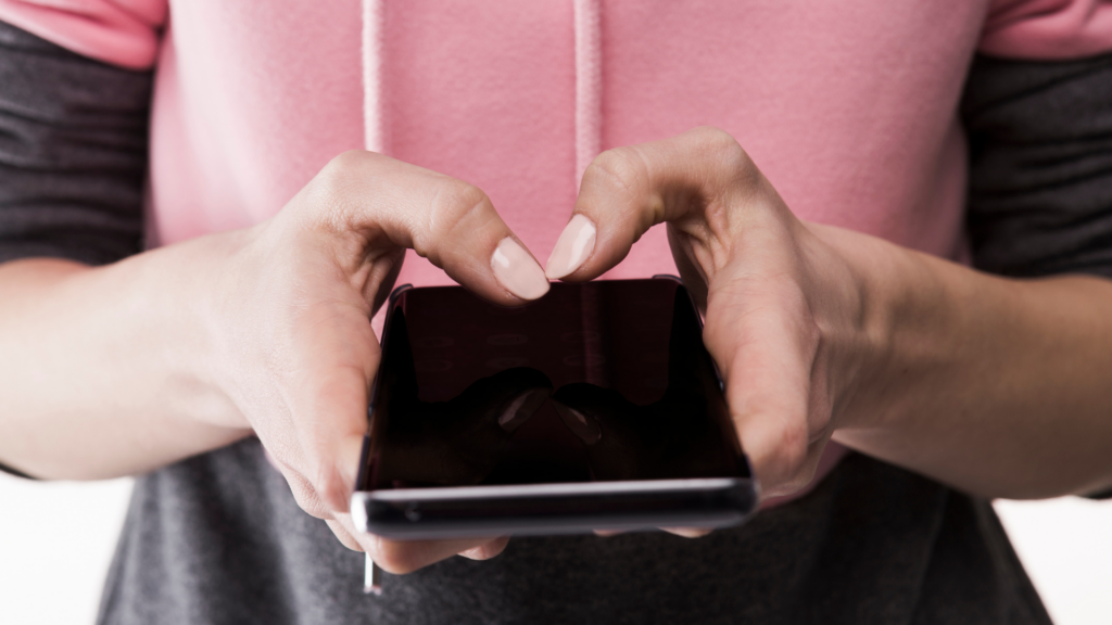 Porównywanie się do innych w mediach społecznościowych – dłonie trzymające smartfon, przeglądanie telefonu zwiększające presję i niezadowolenie z siebie.